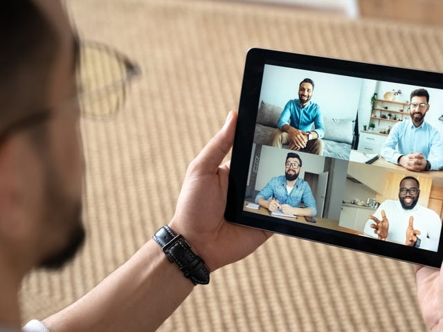 Homme tenant une tablette et discutant avec ses camarades de classe et son formateur lors d'un cours de langue en ligne.