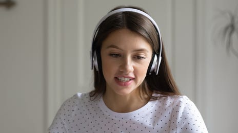 Jeune fille avec des écouteurs parlant à son professeur via son ordinateur portable lors d'un cours de langue en ligne avec Berlitz France.
