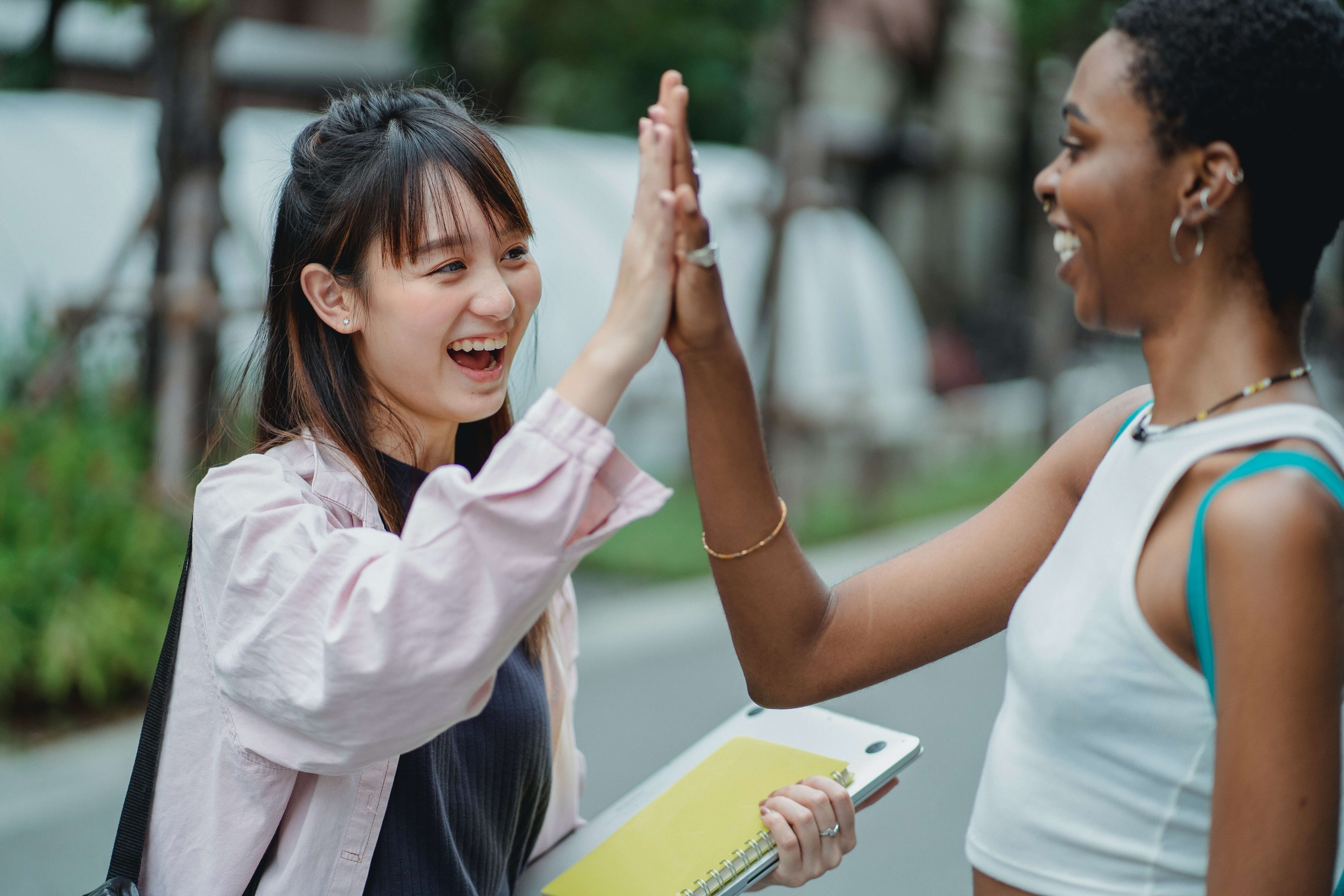 Two women on the street greeting each other with a high five