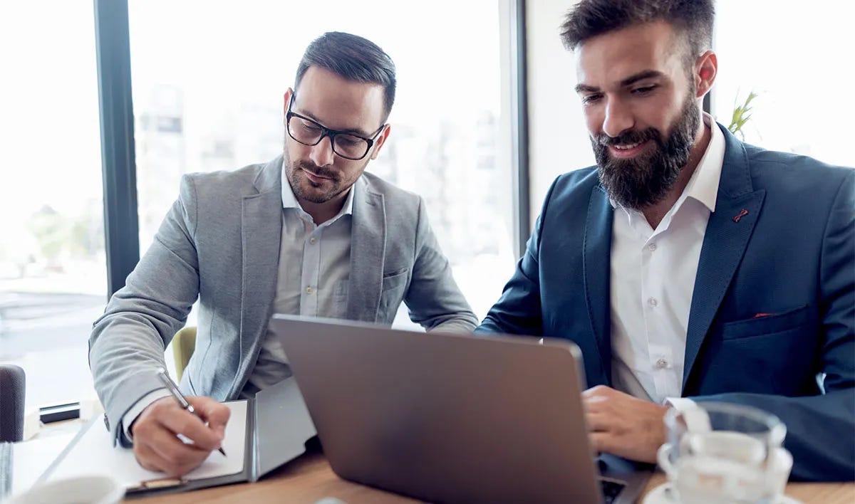 Two men in an office sitting in front of a laptop and putting together a formal letter for work