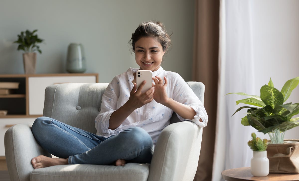 Femme assise confortablement sur un canapé et tenant son téléphone pour apprendre une langue par Skype