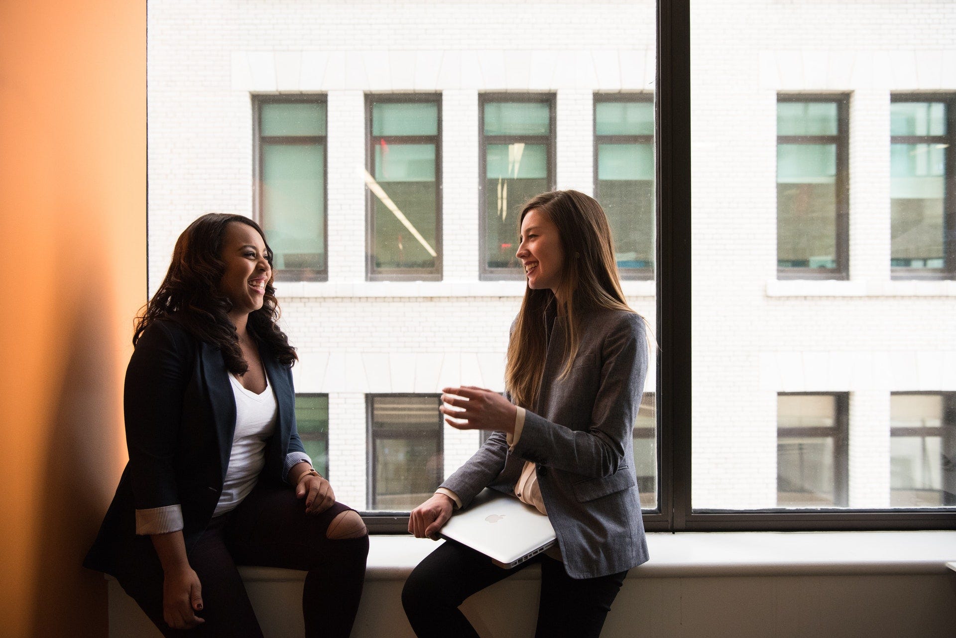 Two women laughing and talking to each other about what happened to them last week