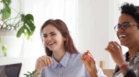 Deux femmes avec des cafés, assises à une table et riant avec leur instructeur lors d'un formation linguistique pour les employés
