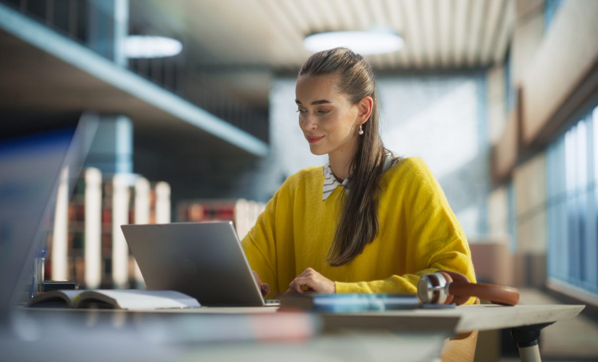 Femme dans une bibliothèque apprenant une nouvelle langue sur son ordinateur avec Berlitz Flex