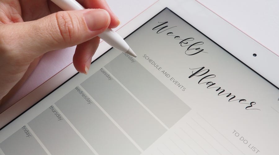 A hand writing in a weekly planner on a tablet