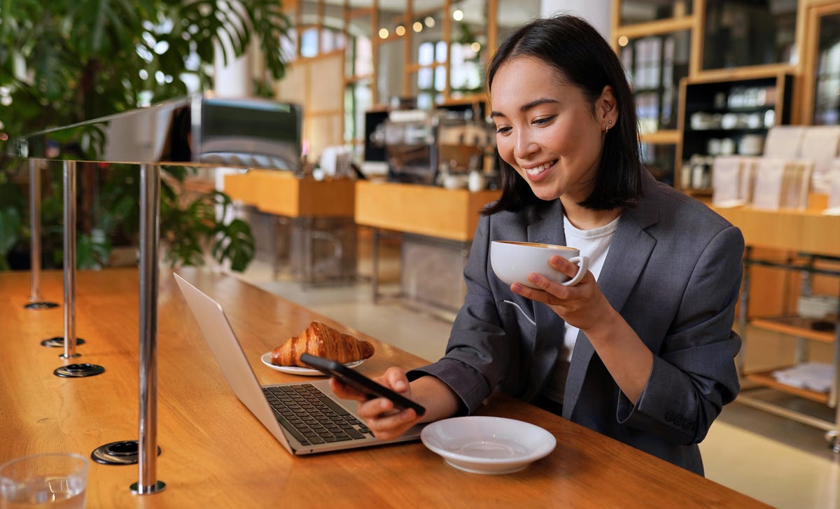 Femme dans un café en train de boire un café et d'apprendre une langue sur son ordinateur portable et son téléphone avec l'aide de Berlitz Connect.