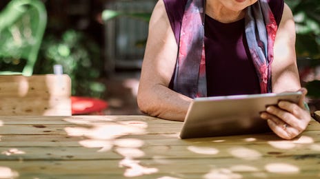 Femme âgée assise à une table, tenant une tablette et suivant une formation anglais á Lille