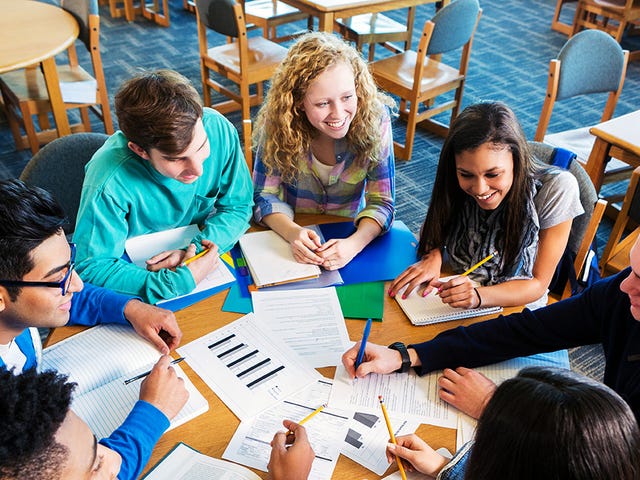 Des enfants et leur instructeur assis autour d'une table avec leurs papiers et discutant pendant un camp sur les Berlitz jobs avec leur instructeur