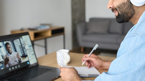 Homme avec des écouteurs, assis à une table et prenant des notes pendant un cours en ligne