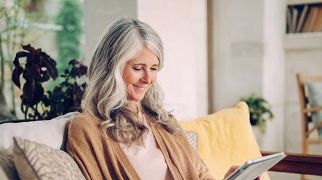 Femme sur un canapé tenant une tablette dans les mains et suivant un cours d'anglais á Strasbourg depuis son salon.