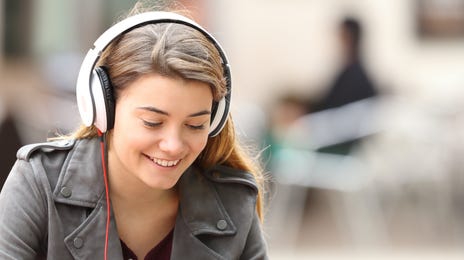 Jeune femme avec des écouteurs, assise à l'extérieur avec sa tablette et faisant des exercices de langue en ligne avec Berlitz Flex