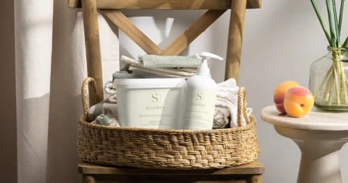 Productos de lavandería Scentsy exhibidos en una canasta tejida con ropa doblada en un ambiente hogareño natural y suave.