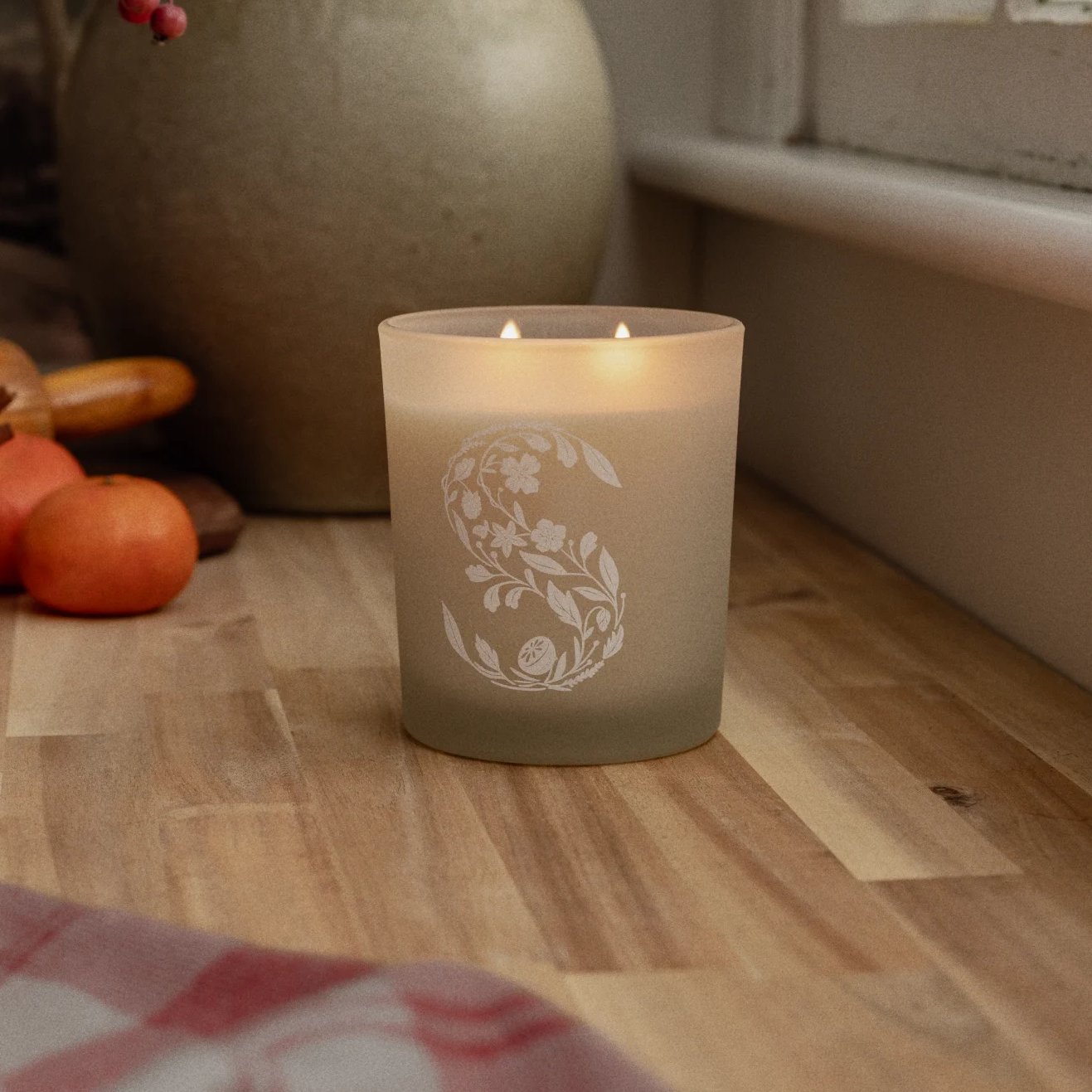 A Scentsy Candle sits on a wood slab kitchen counter surrounded by decor and fruits