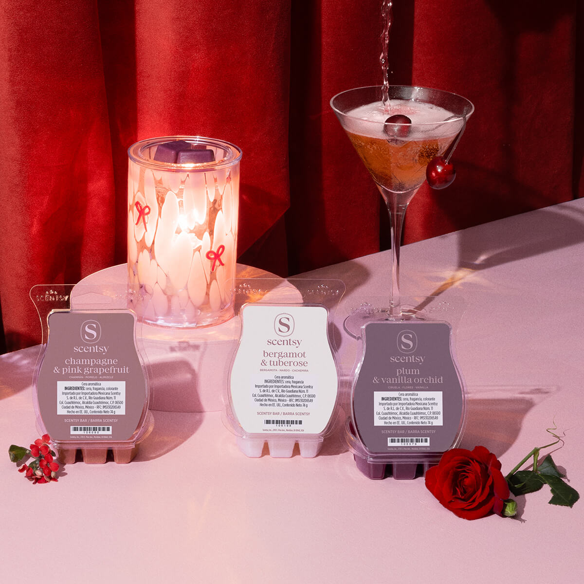 Los productos de la Colección del Día de San Valentín se muestran en una mesa rosa entre flores y vasos llenos de una bebida espumante en frente de una cortina roja.