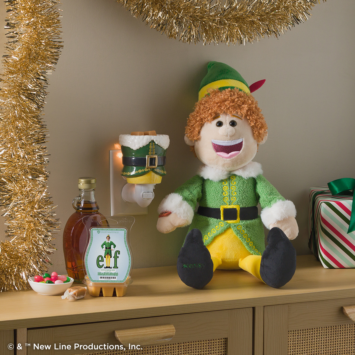 Elf Scentsy Buddy with an Elf mini warmer and Scentsy Bar, styled on a festive shelf with gold tinsel, maple syrup, a bowl of candy and a striped wrapped gift