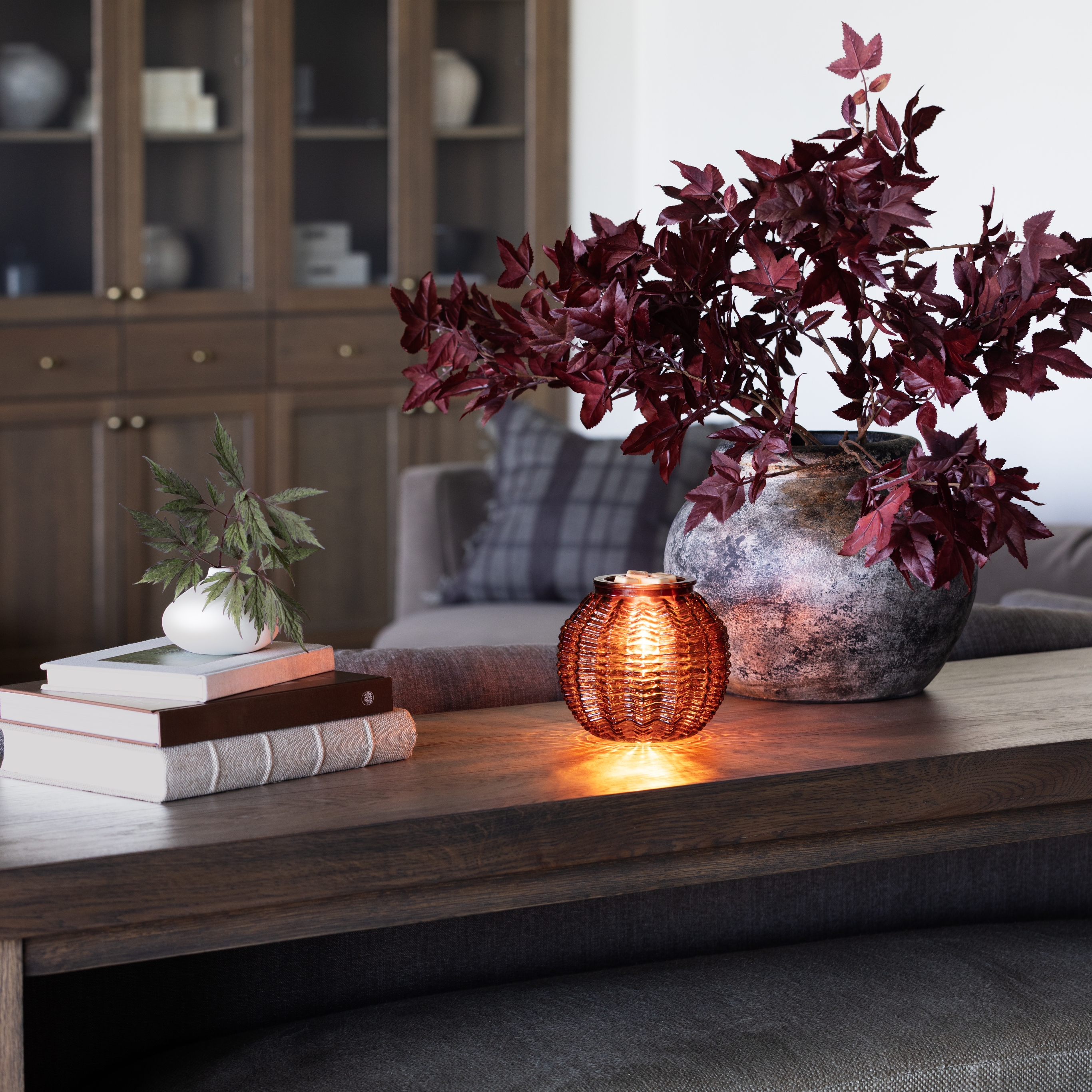 Scentsy Amber Waves Warmer on a table, glowing from within, sitting next to a stack of books and potted plants,