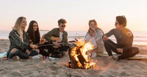  Friends gathered around a bonfire at the beach, roasting marshmallows, playing guitar, and smiling