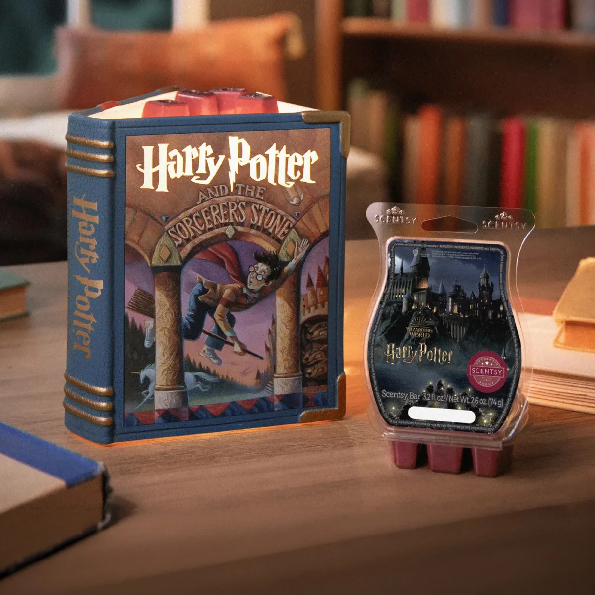 A Harry Potter and the Sorcerer’s Stone – Scentsy Warmer and Wizarding World: Harry Potter – Scentsy Bar sit on a coffee table among books in a reading nook. 