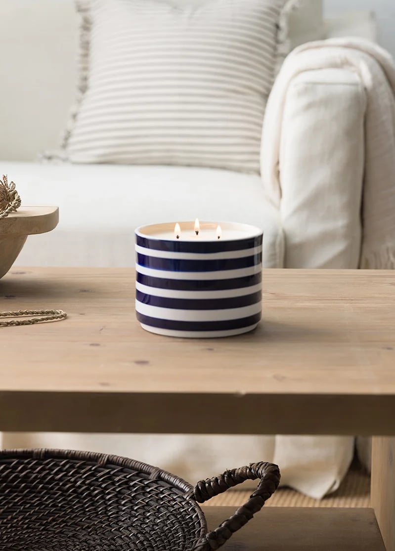 A Barefoot Beach Scented Candle is displayed on a table in a living room setting.