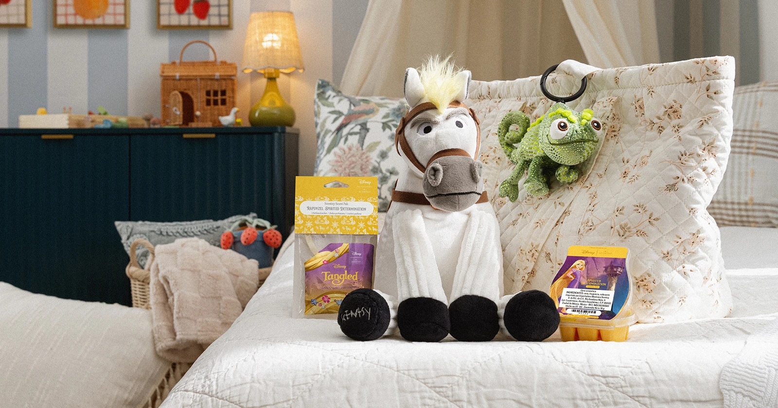 Un Scentsy Buddy – Disney Maximus sentado en una cama con un Sachet Perfumado y una Barra Scentsy – Disney Rapunzel: Spirited Determination todos juntos a un Scentsy Buddy Clip – Disney Pascal enganchado en una bolsa.