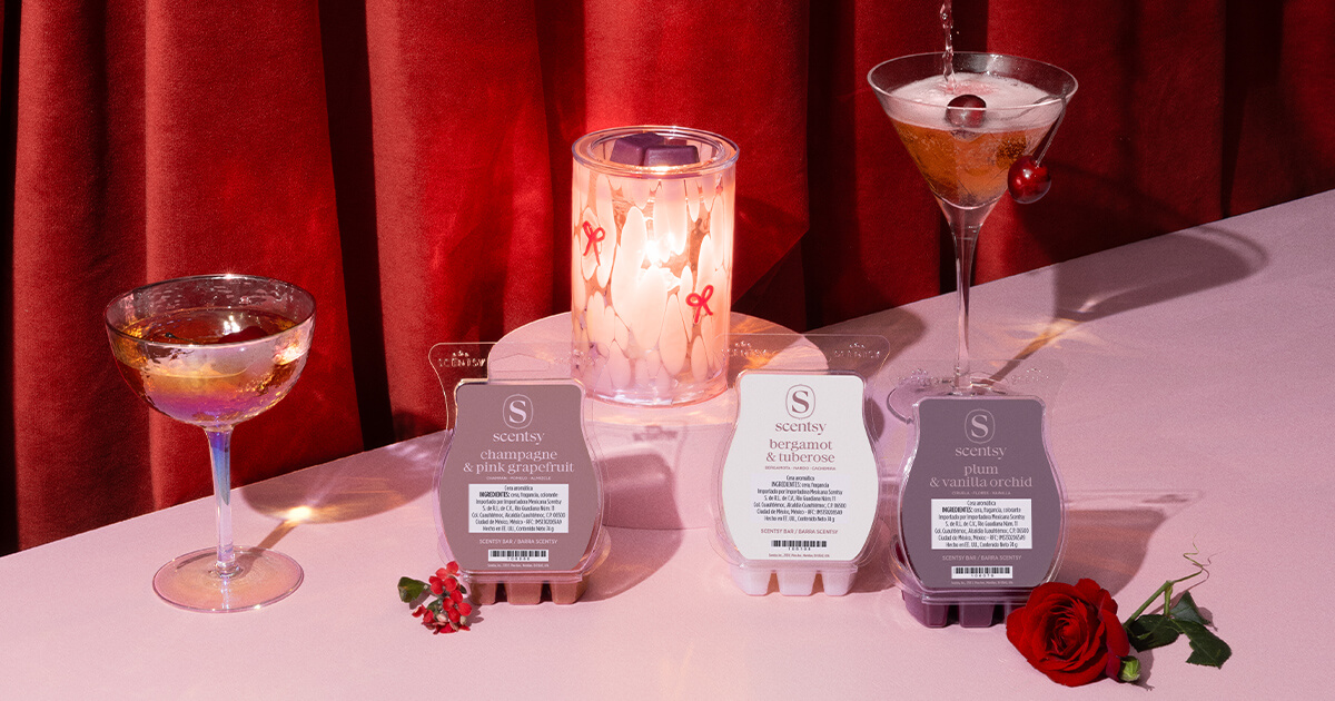 Valentine’s Day Collection featuring the Adorned Affair Warmer, First Blush Warmer, Valentine’s Day 3-Bar Bundle, and Petals & Poems Scented Candle styled with pink cocktails in front of red velvet curtains.