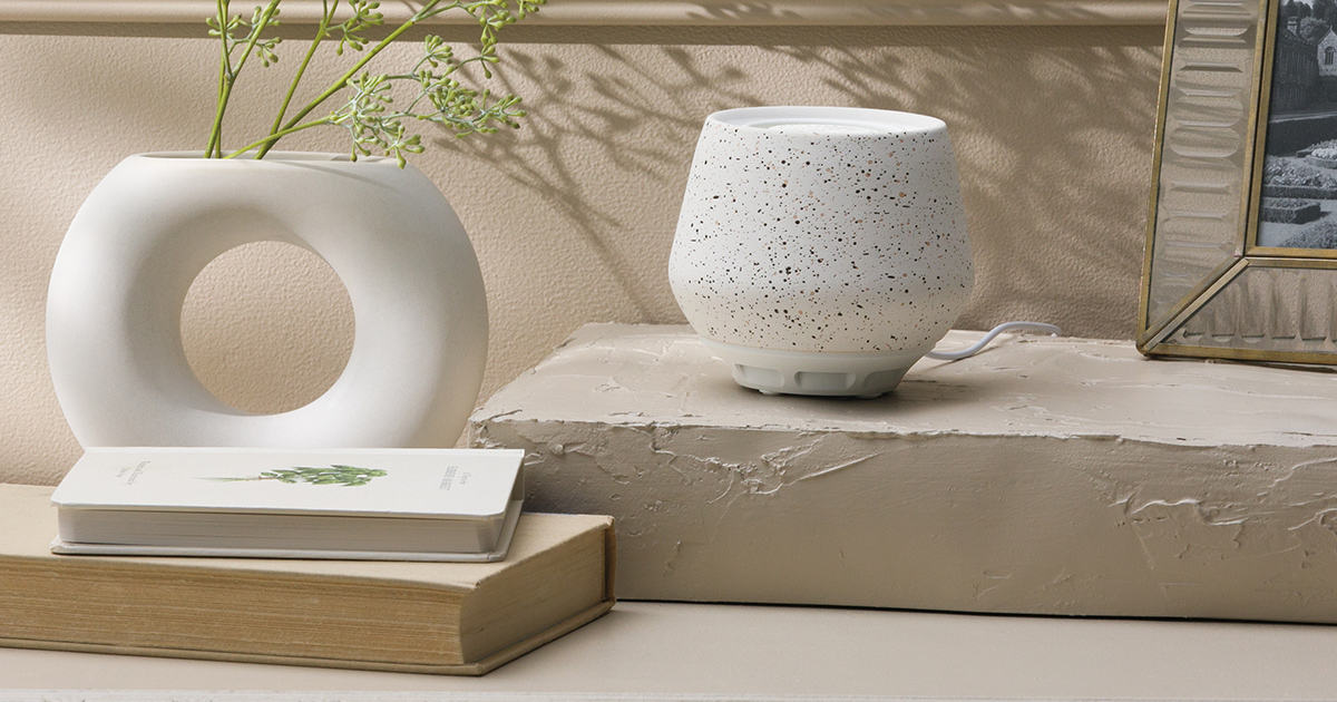 White speckled Tabletop Fan Diffuser with rounded bowl shape on textured gray pedestal, styled with circular vase, books, and gold-framed mirror on neutral surface