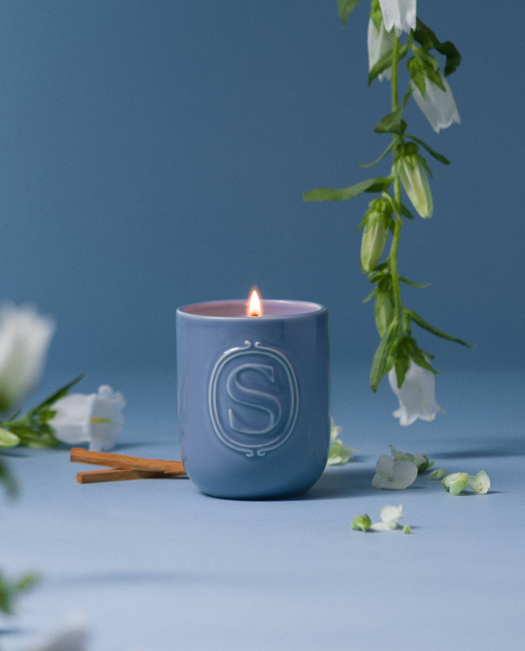 Scentsy Firewood Spruce Candle in a glass jar, surrounded by snowflakes, pine needles, and wood shavings on a blue background.