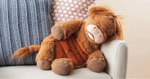 Hamish the Highland Cow Weighted & Warming Scentsy Buddy plush sitting on a chair in a cozy home setting.