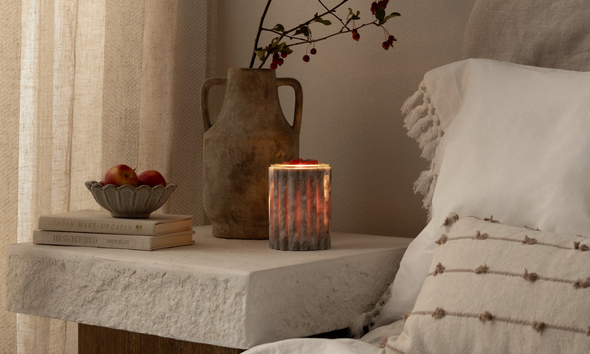 Cascade Warmer in matte white ceramic with soft sculpted curves, styled on a wooden console table beside greenery and decorative accents in a warm, neutral home setting.