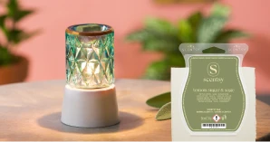 A lit Crowned in Gold Mini Warmer is displayed with plants and a Lemon Sugar & Sage Scentsy Bar on a wood table.