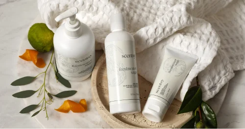 Scentsy body care products displayed on a soft towel with natural accents in a bright, spa-inspired setting.