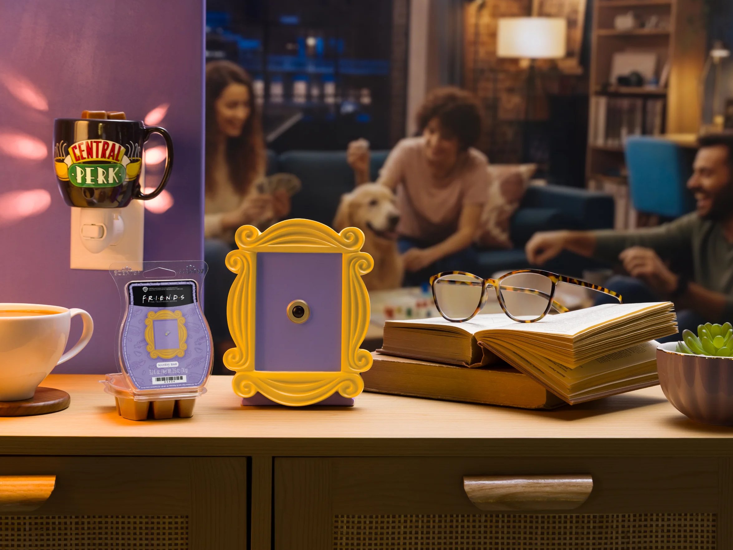Friends Collection products are displayed with a coffee cup, books and eyeglasses. People socialize in the background. 