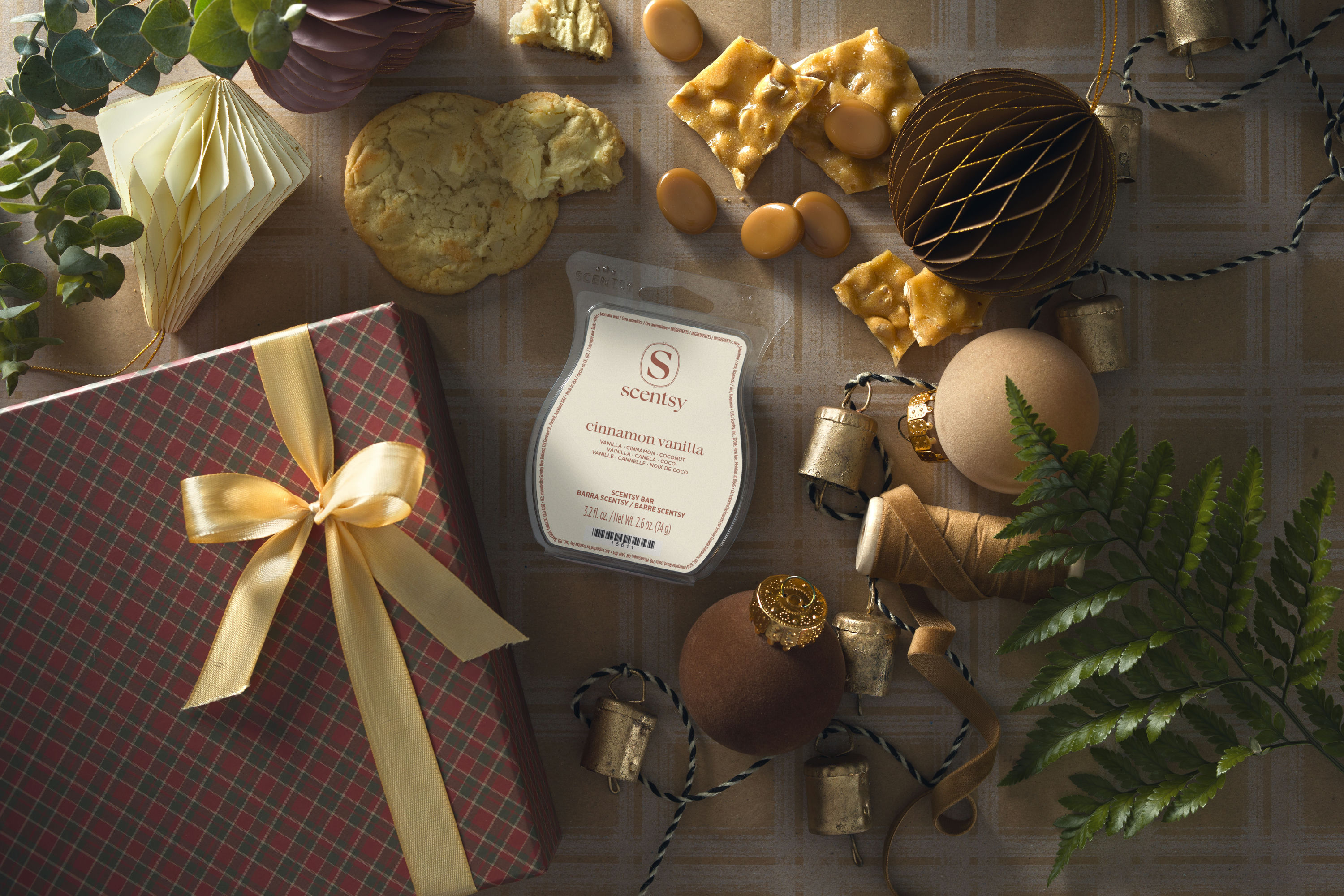 Barra de cera Scentsy Cinnamon Vanilla estilizada con galletas navideñas, caramelos, turrón de cacahuate, un regalo envuelto, adornos y campanas.