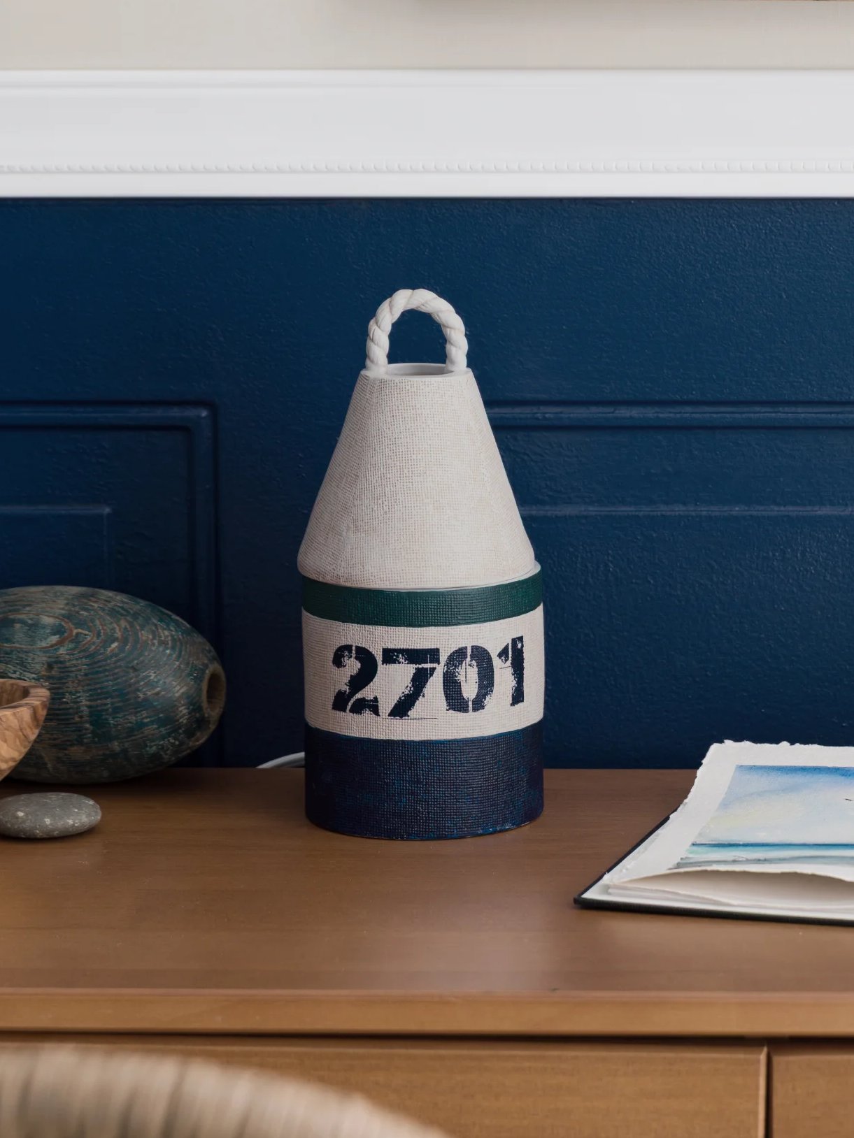 A Bay Buoy Warmer is displayed on a desk next to a notebook and coastal décor.
