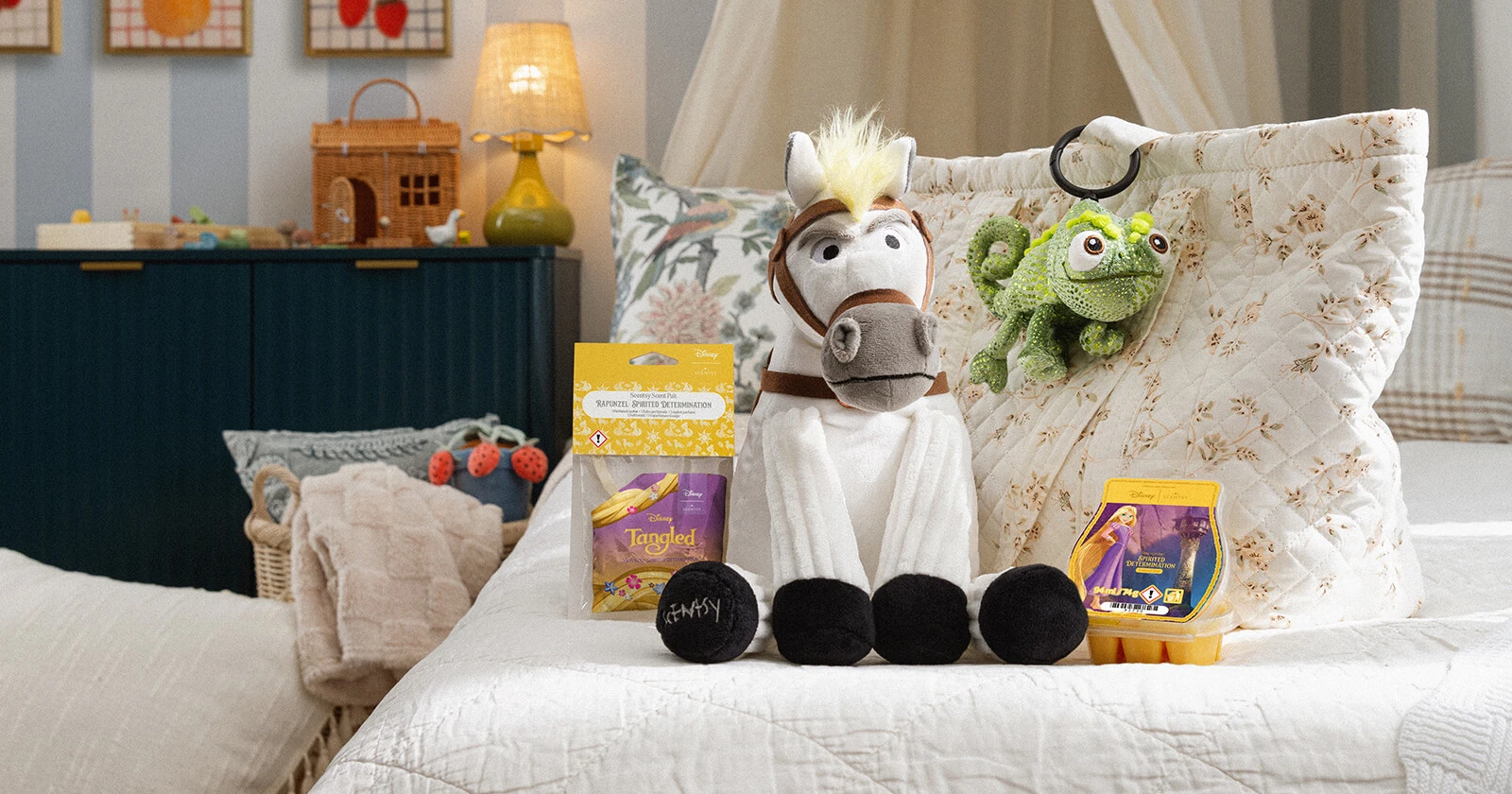 A Disney Maximus – Scentsy Buddy sits on a bed with a Disney Rapunzel: Spirited Determination – Scent Pak and Scentsy Bar near a Disney Pascal – Scentsy Buddy Clip clipped to a bag.