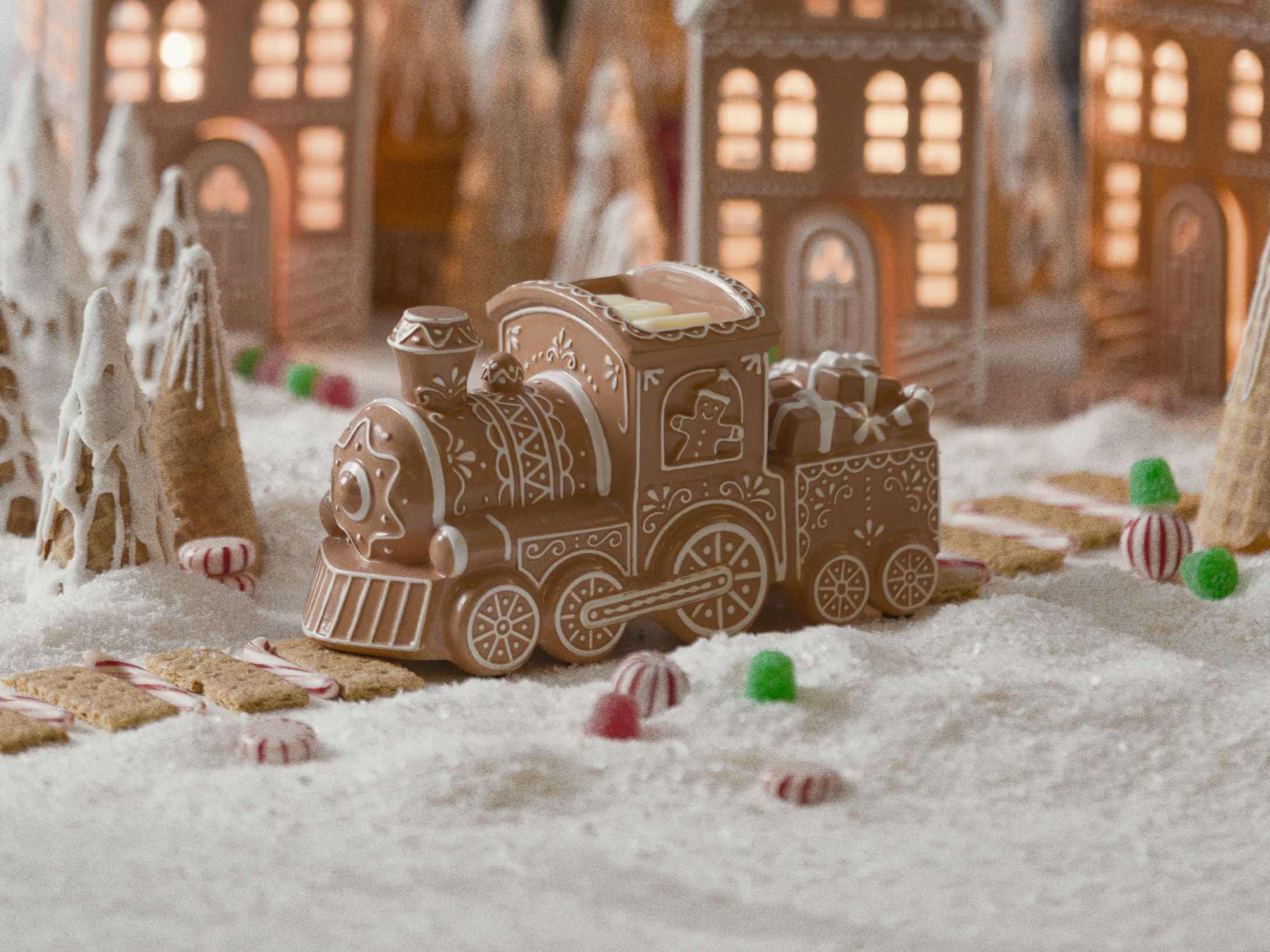 A gingerbread train Scentsy Warmer rolls through a snowy gingerbread village scattered with peppermints and gumdrops.