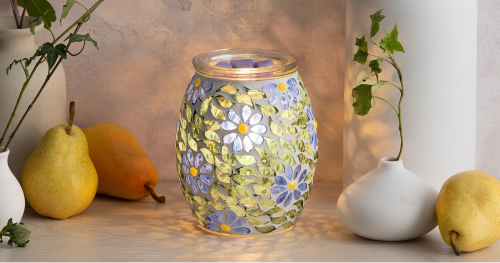 Scentsy Warmer with purple and white floral mosaic pattern and yellow centers, illuminated from within, displayed on wood surface with pears and white ceramic vases
