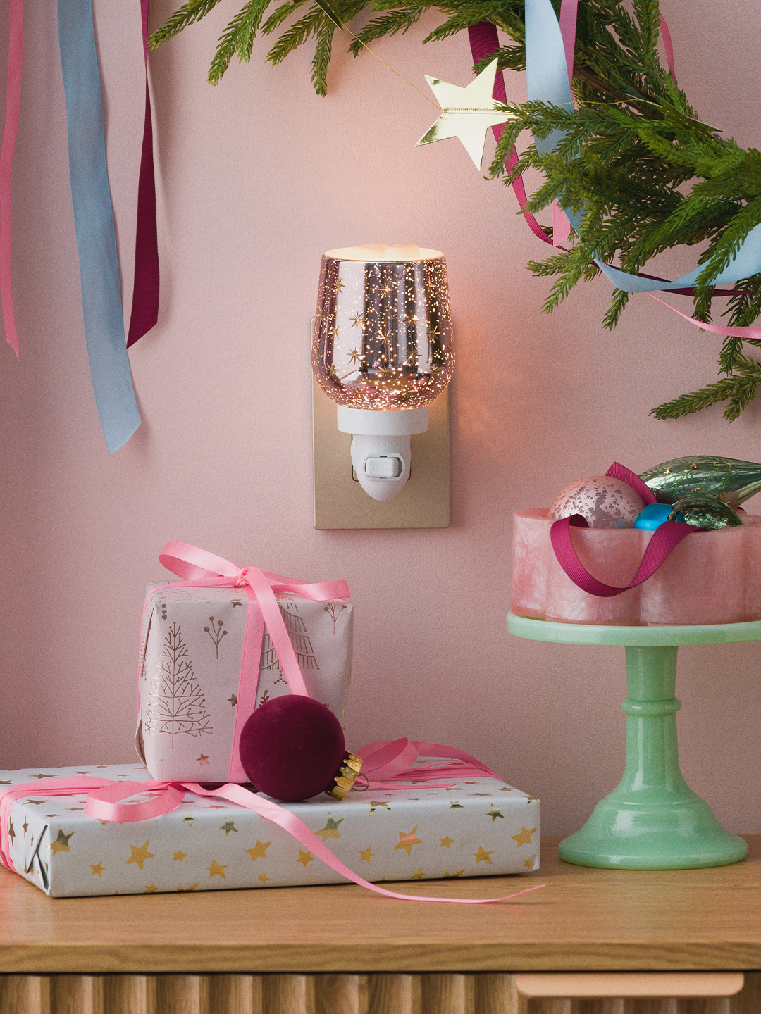 Eine Elektrische Miniduftlampe Frosted Flurry ist inmitten von Weihnachtsdekoration an eine Steckdose angeschlossen.