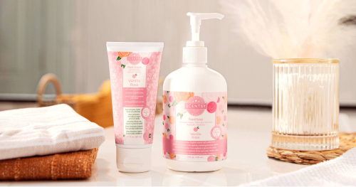 Scentsy Vanilla Rose body wash in white bottle with pink floral label on gray countertop, styled with wooden brush, pink flowers, and blurred bathroom accessories