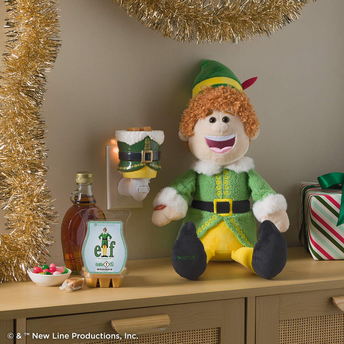 Elf Scentsy Buddy with an Elf mini warmer and Scentsy Bar, styled on a festive shelf with gold tinsel, maple syrup, a bowl of candy and a striped wrapped gift