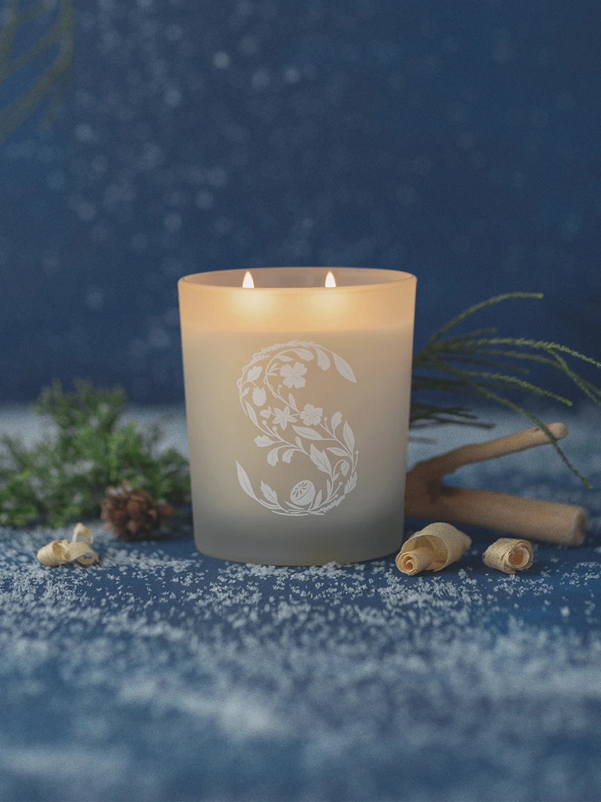 Scentsy Firewood Spruce Candle in a glass jar, surrounded by snowflakes, pine needles, and wood shavings on a blue background.