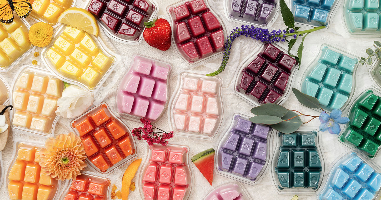 Un colorido surtido arcoíris de barras de cera Scentsy estilizado con flores frescas, cítricos y bayas.