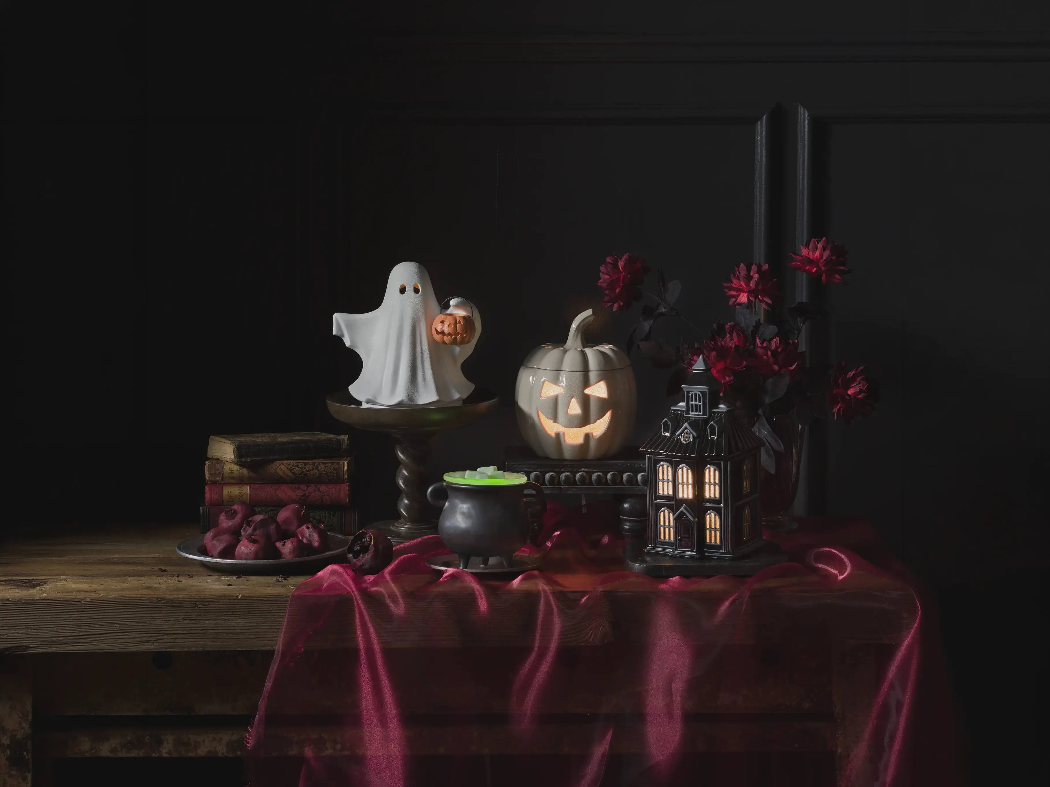 Halloween Edit Warmers on display in a dark, haunting setting with black and red accents, antique books and dried fruit.