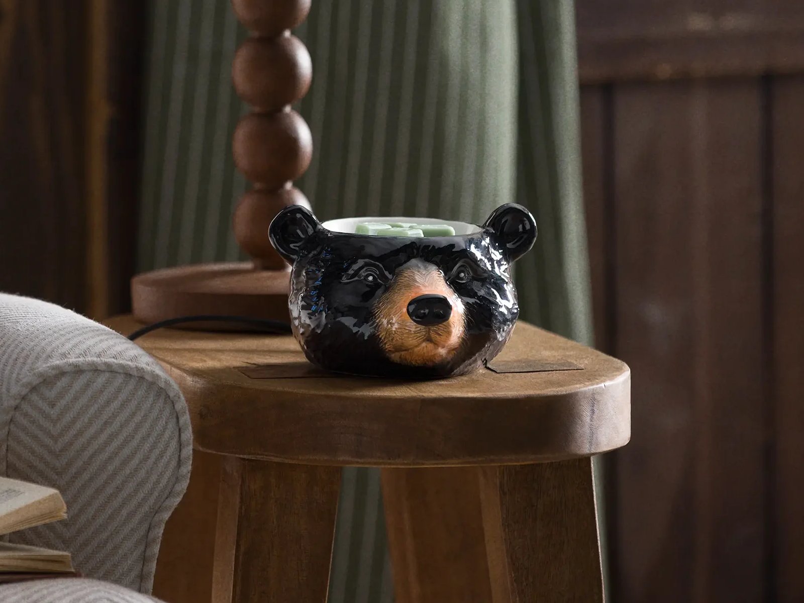 Cozy Cabin Edit Warmers on display in a rustic cabin setting with evergreen and pinecones, a fish painting and a window to the lake outside.