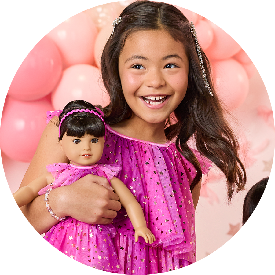 Young girl holding her doll in matching pink dress