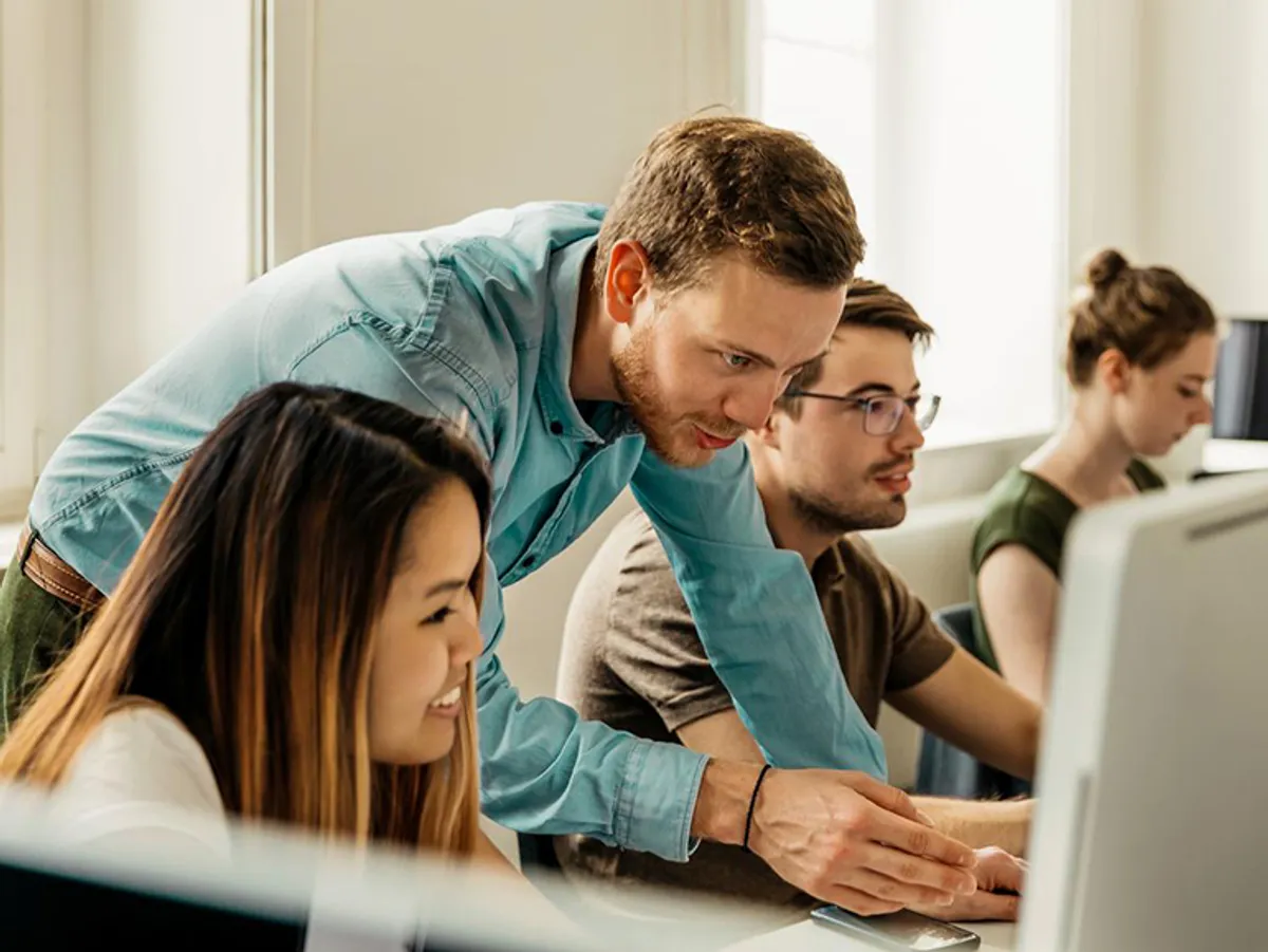 A teacher assists students working on computers in a classroom.