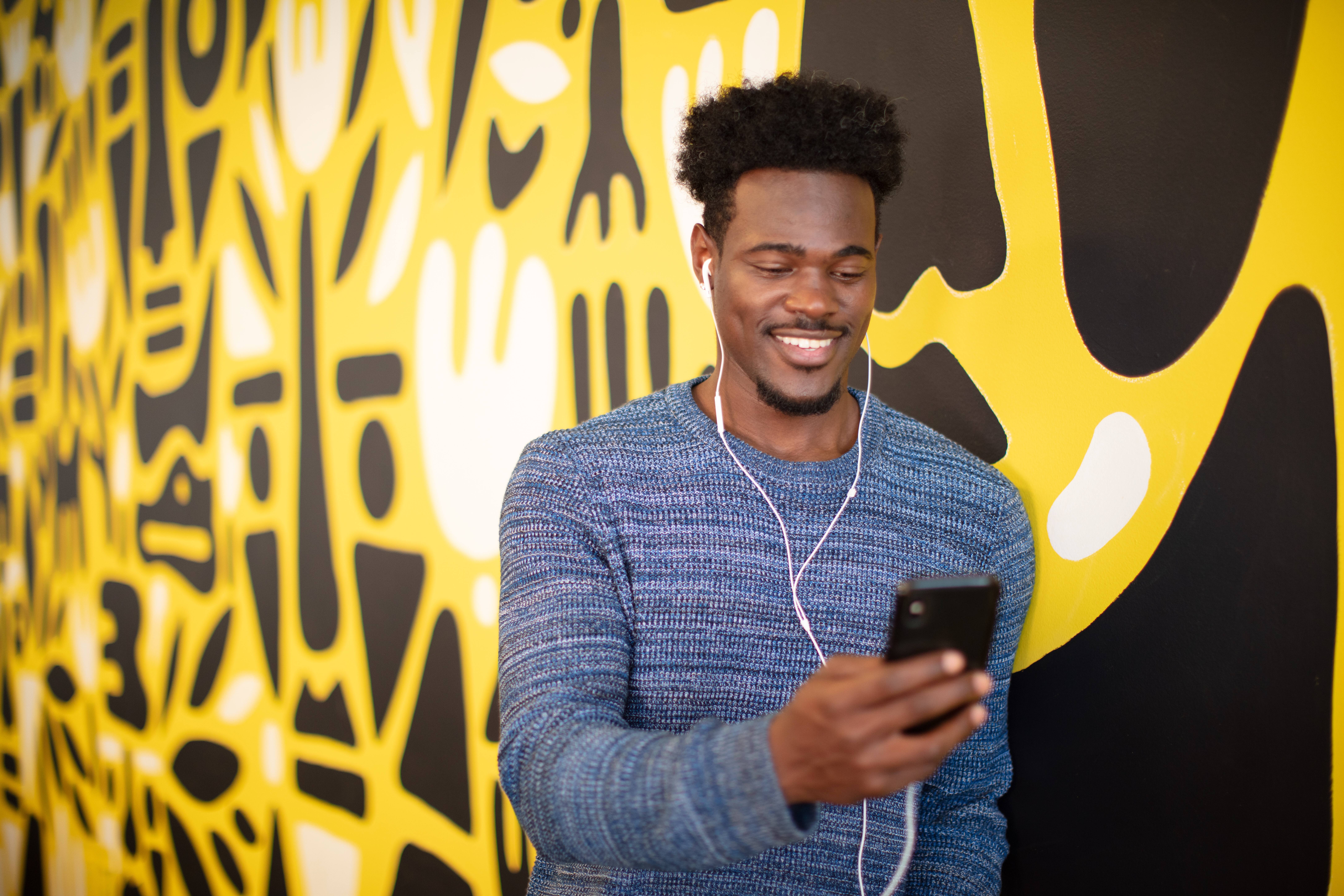 A young male wearing hands-free smiling at his phone screen using 8x8 work to communicate