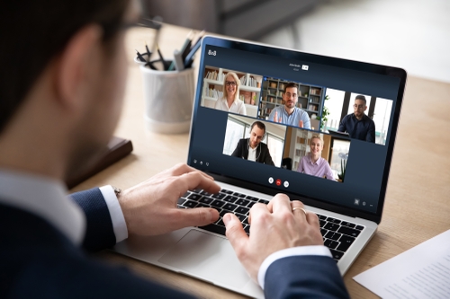 An office employee using 8x8 work on his laptop to connect with and see his five colleagues via video call