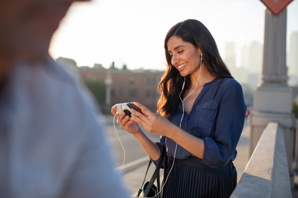 A young female wearing a blue shirt smiling at her phone screen, using handsfree to communicate via 8x8 chat.