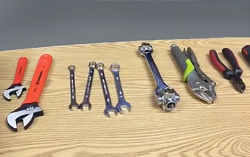 A set of tools, including various wrenches and pliers, on a wooden table.  
